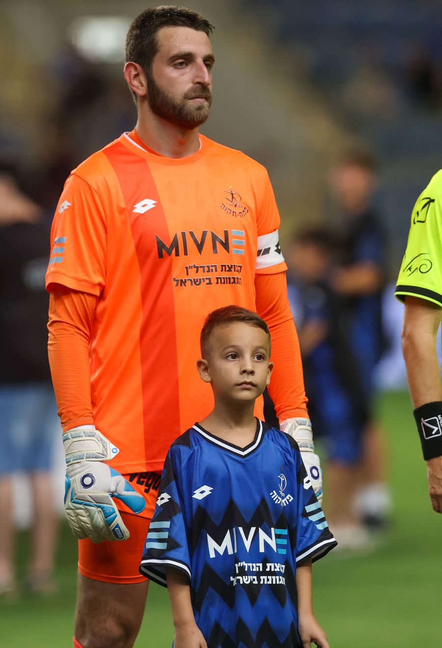 A young boy stands next to an adult player, both wearing team kits
