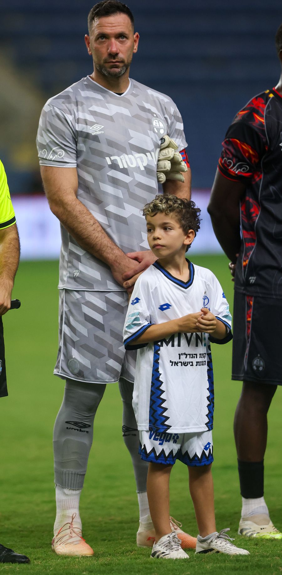 Ofir Marciano (Hapoel Beer Sheva) A young boy stands next to a goalkeeper, both looking towards the camera.
