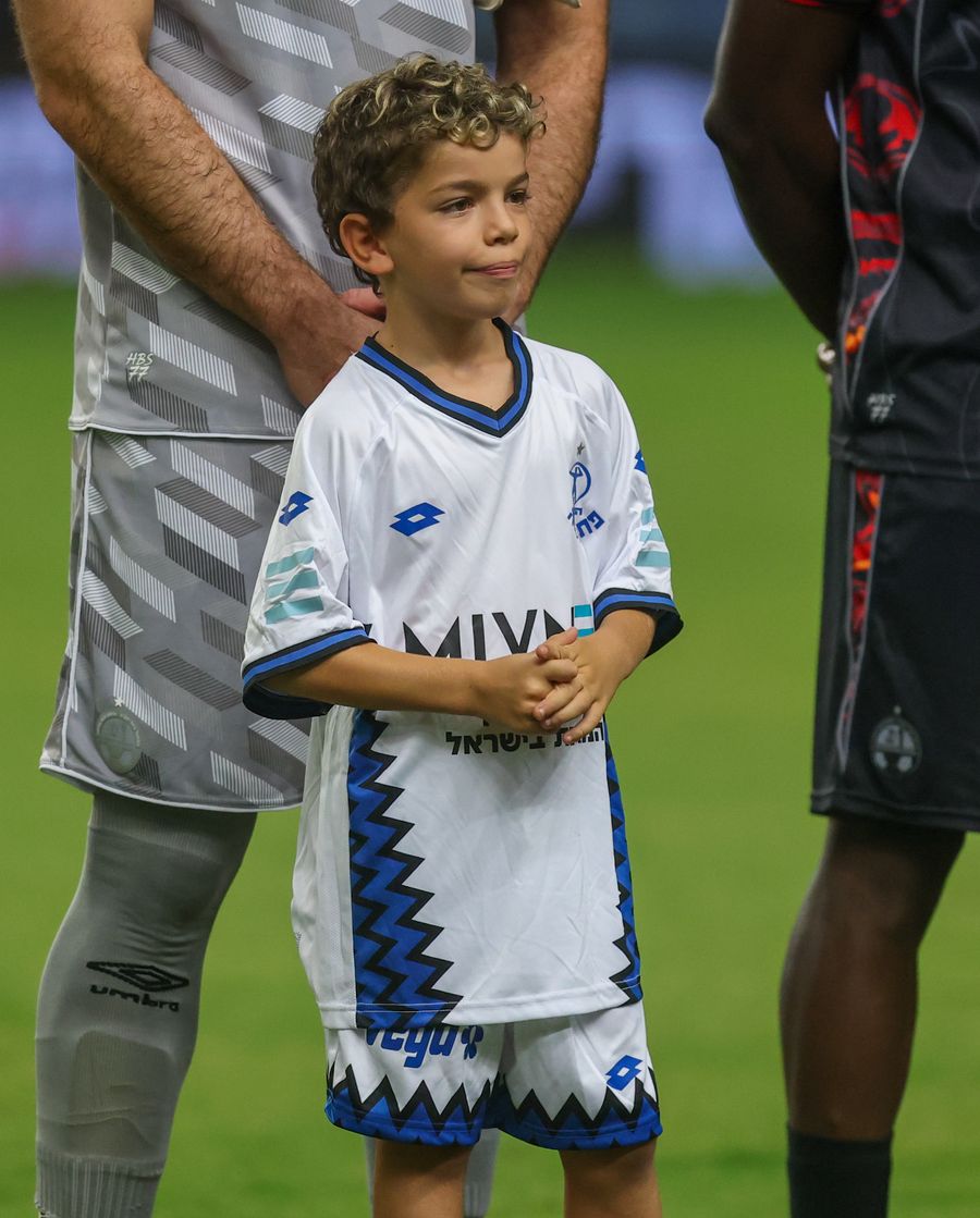 A young boy standing on a football field with two adults behind him