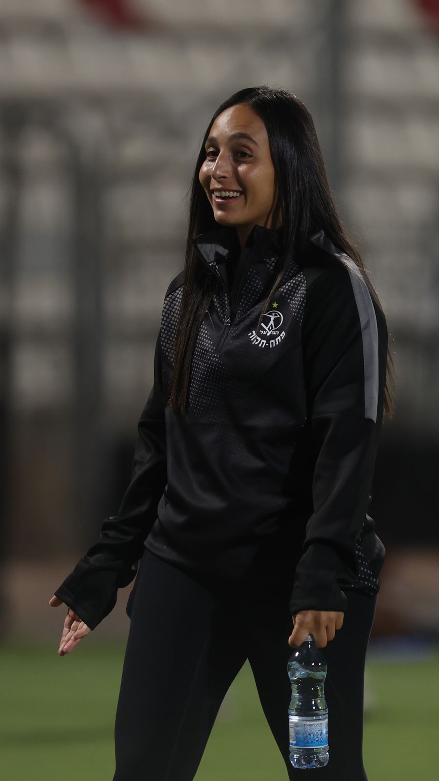 A woman is walking on the field, holding a bottle of water
