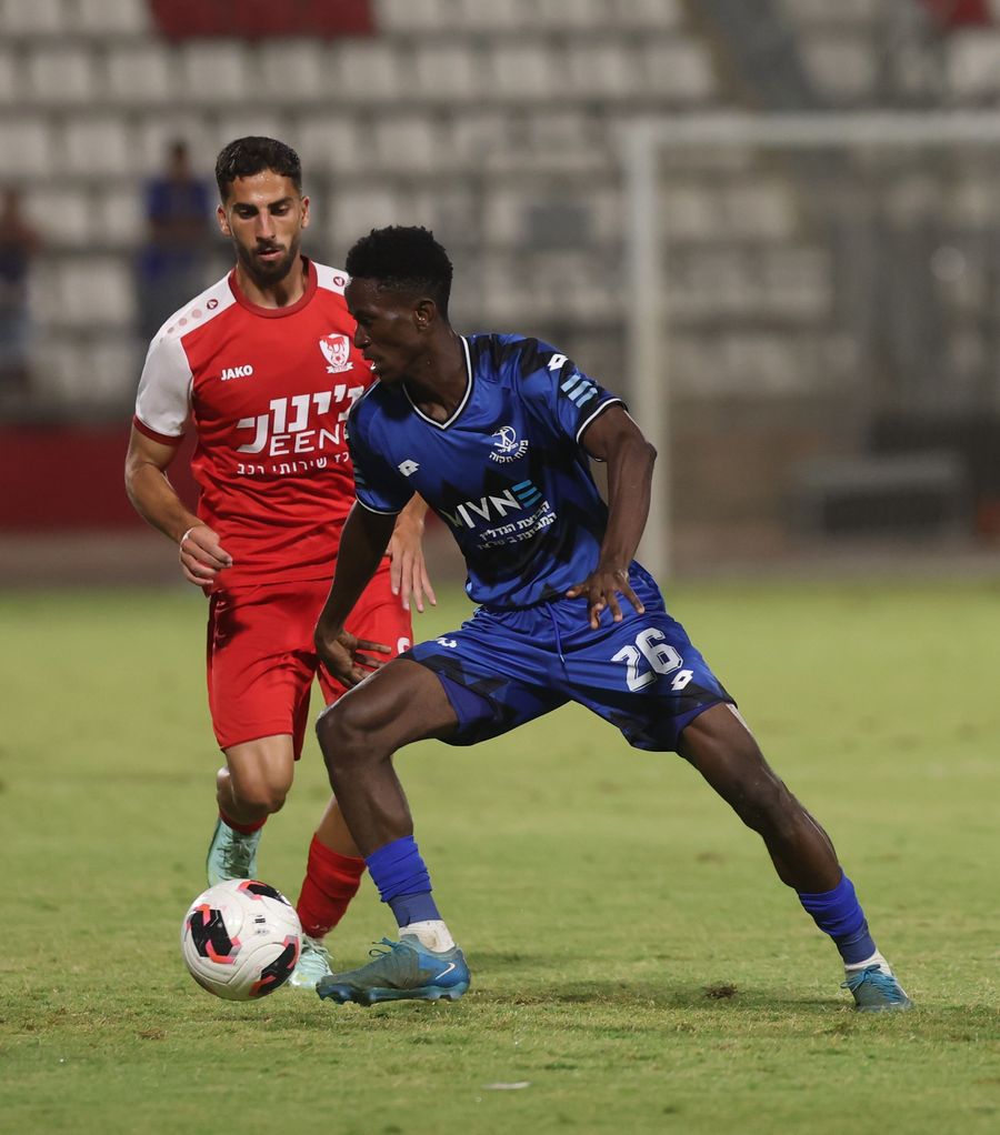 Ahmed Taha (Bnei Sakhnin) controls the ball as Karim Kimvuidi (Hapoel Petah Tikva) chases the ball