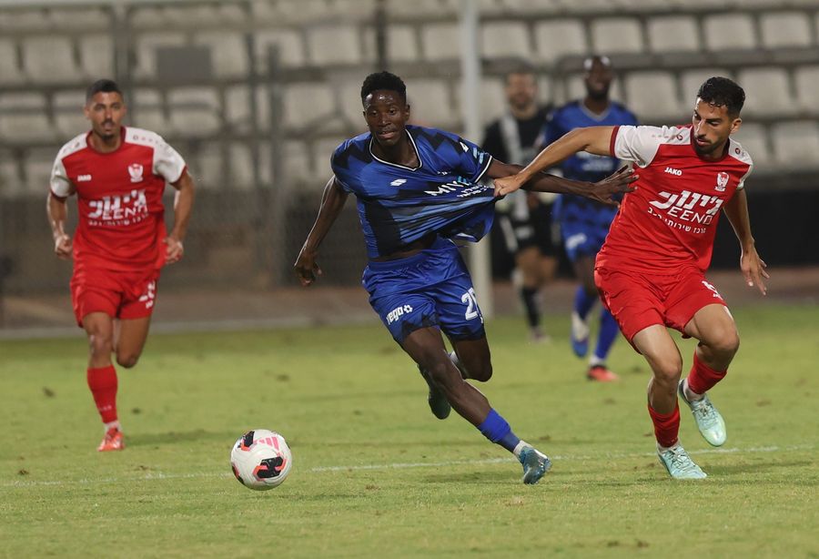 Ilay Hajaj (Bnei Sakhnin) runs with the ball as Karim Kimvuidi (Hapoel Petah Tikva) defends against the player in blue