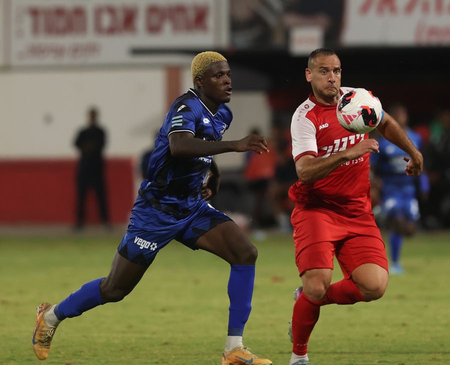 Iyad Abu Abaid (Bnei Sakhnin) controls the ball with his right foot as Yves Erick Bile (Hapoel Petah Tikva) sprints towards the ball
