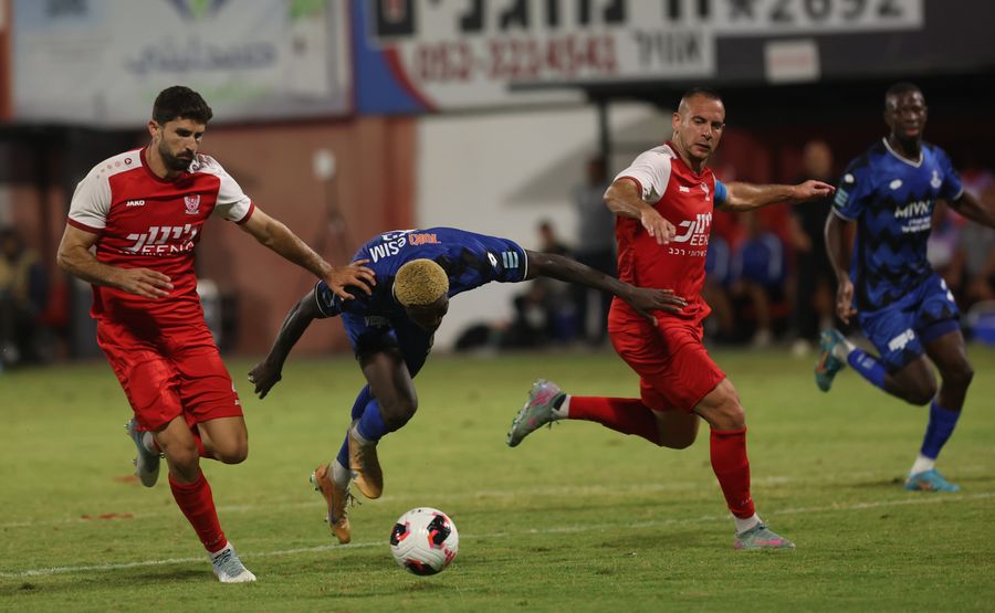 A footballer is tackling a player in a blue kit during a football match