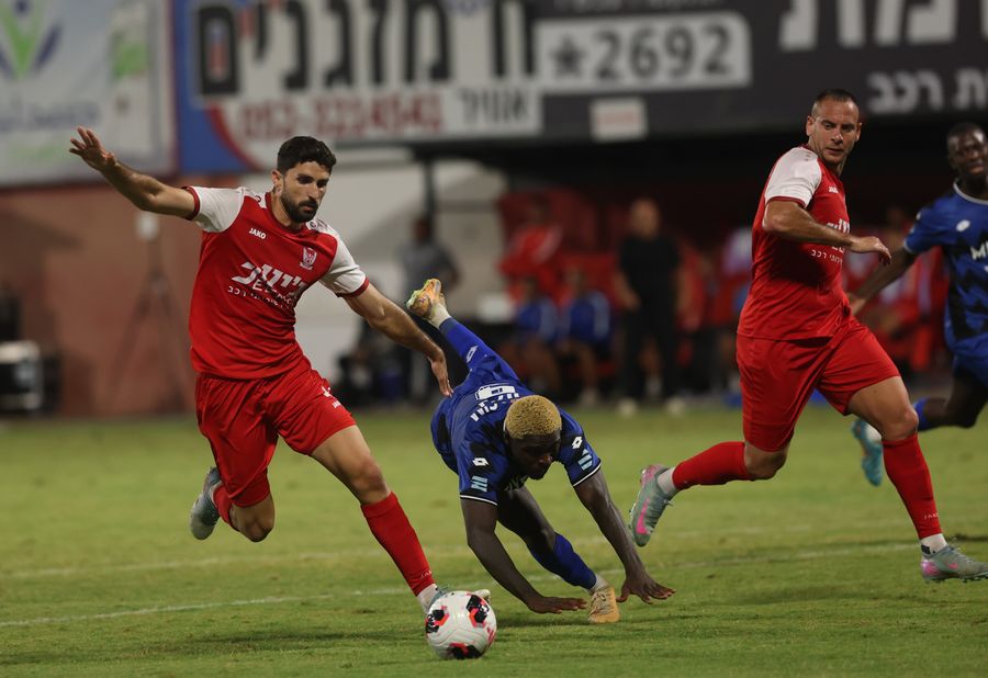 Yves Erick Bile (Hapoel Petah Tikva) slides to block the ball as Ori Dahan (Bnei Sakhnin) runs towards the ball