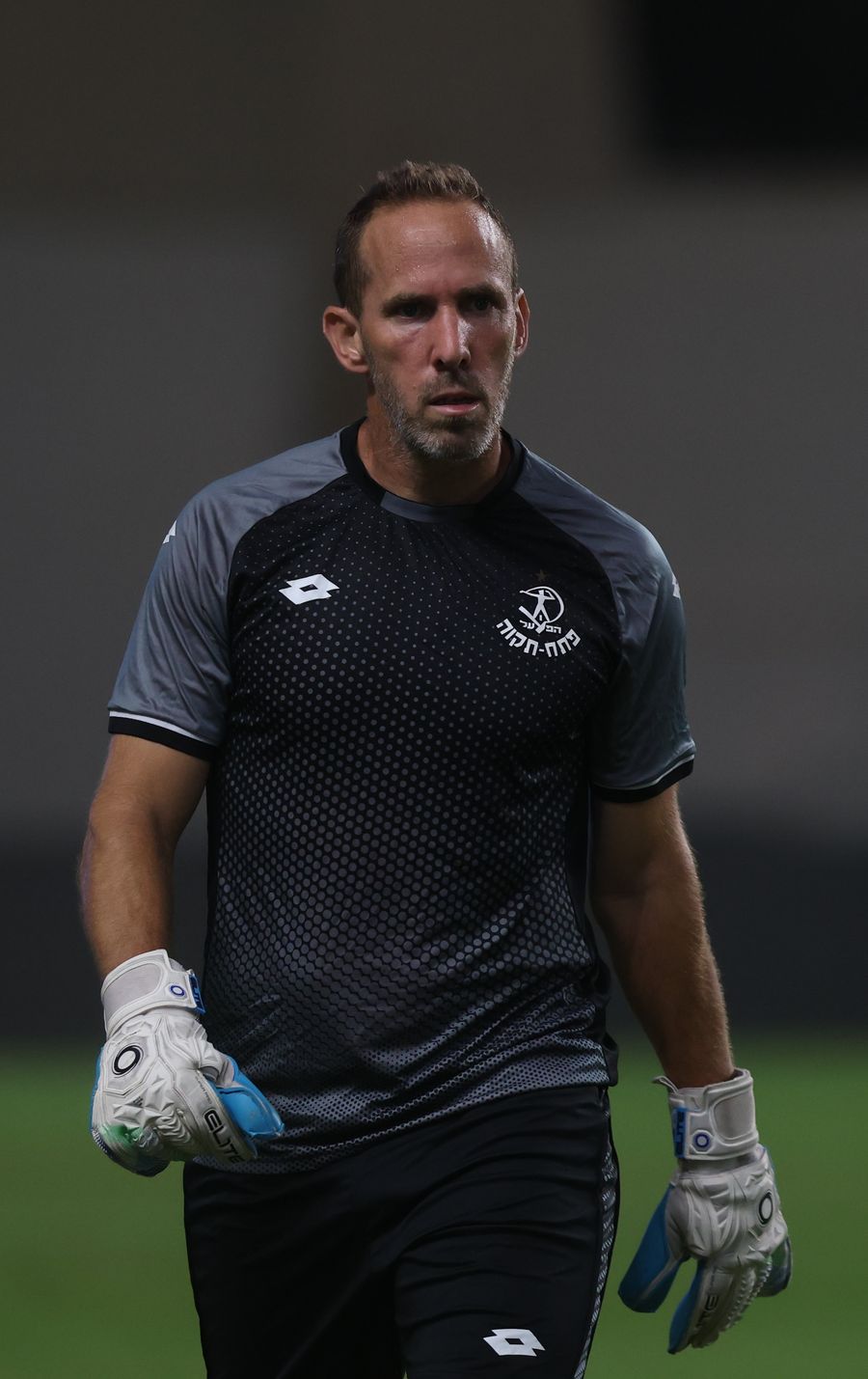 A footballer Goalkeeper standing with hands on hips, possibly during a break in play.