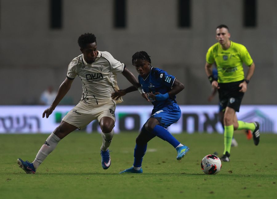 A Hapoel Petah Tikva player is defending against an opponent in a blue kit who is attempting to control the ball