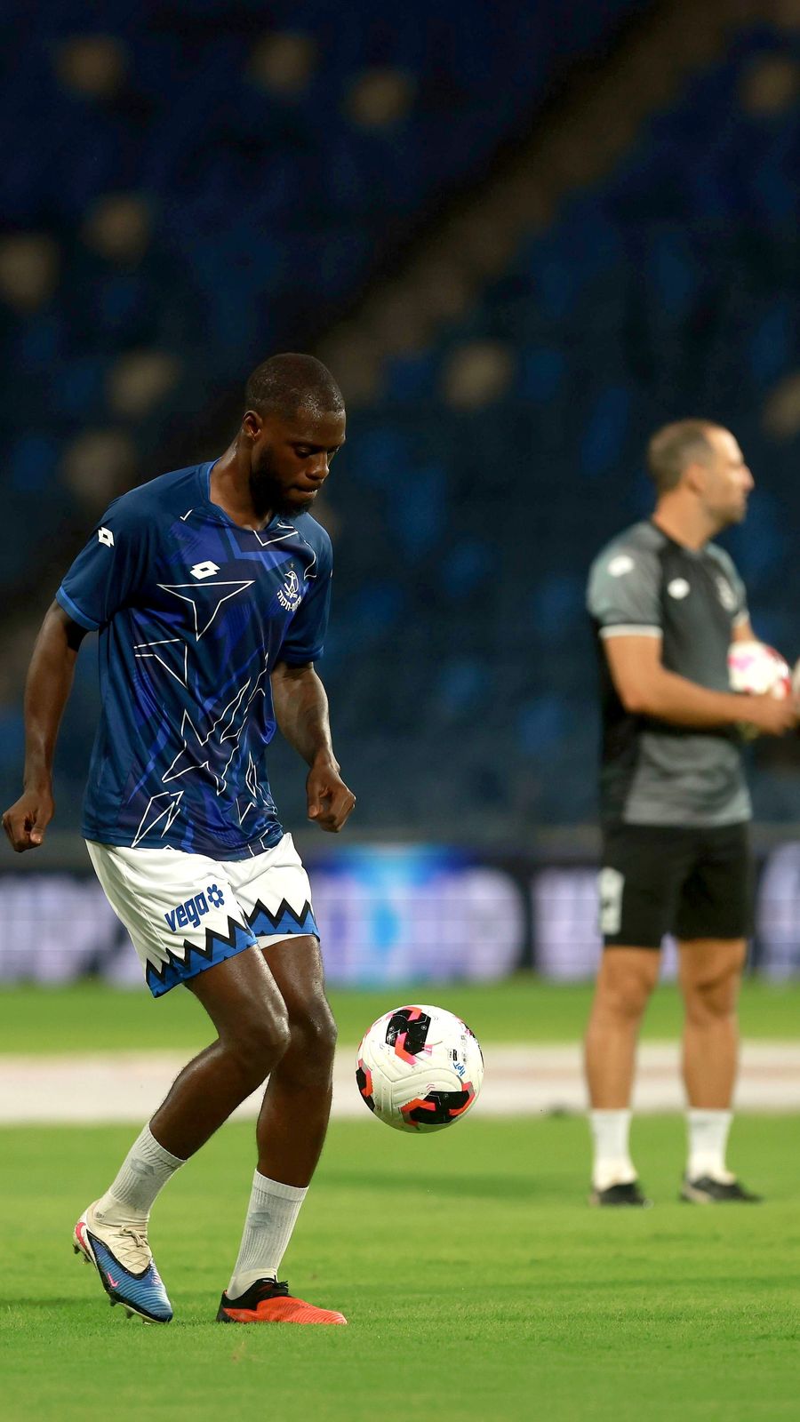 Alex Moussounda (Hapoel Petah Tikva) is controlling the ball with his right foot while a coach in grey and black observes