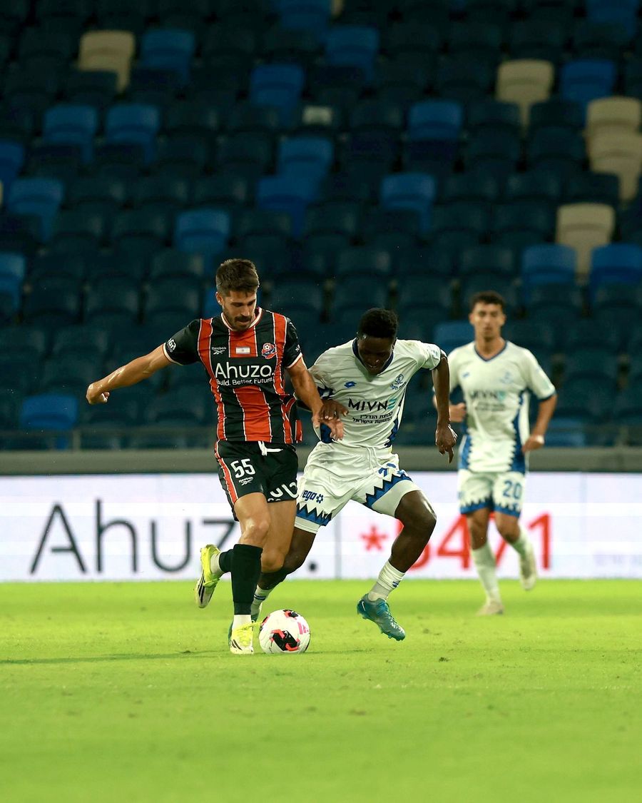 Karim Kimvuidi (Hapoel Petah Tikva) controls the ball and dribbling as Naor Sabag (#55, Hapoel Haifa) is attempting to block the ball from the opponent