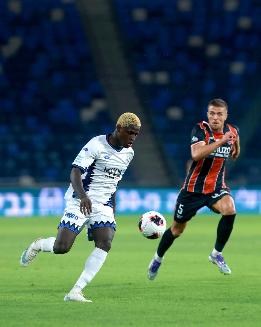 Ivan Kričak (Hapoel Haifa) strikes the ball with his right foot as Yves Erick Bile (Hapoel Petah Tikva) runs towards the ball